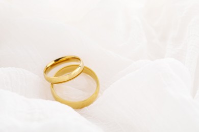 Photo of Beautiful golden wedding rings on white fabric, space for text