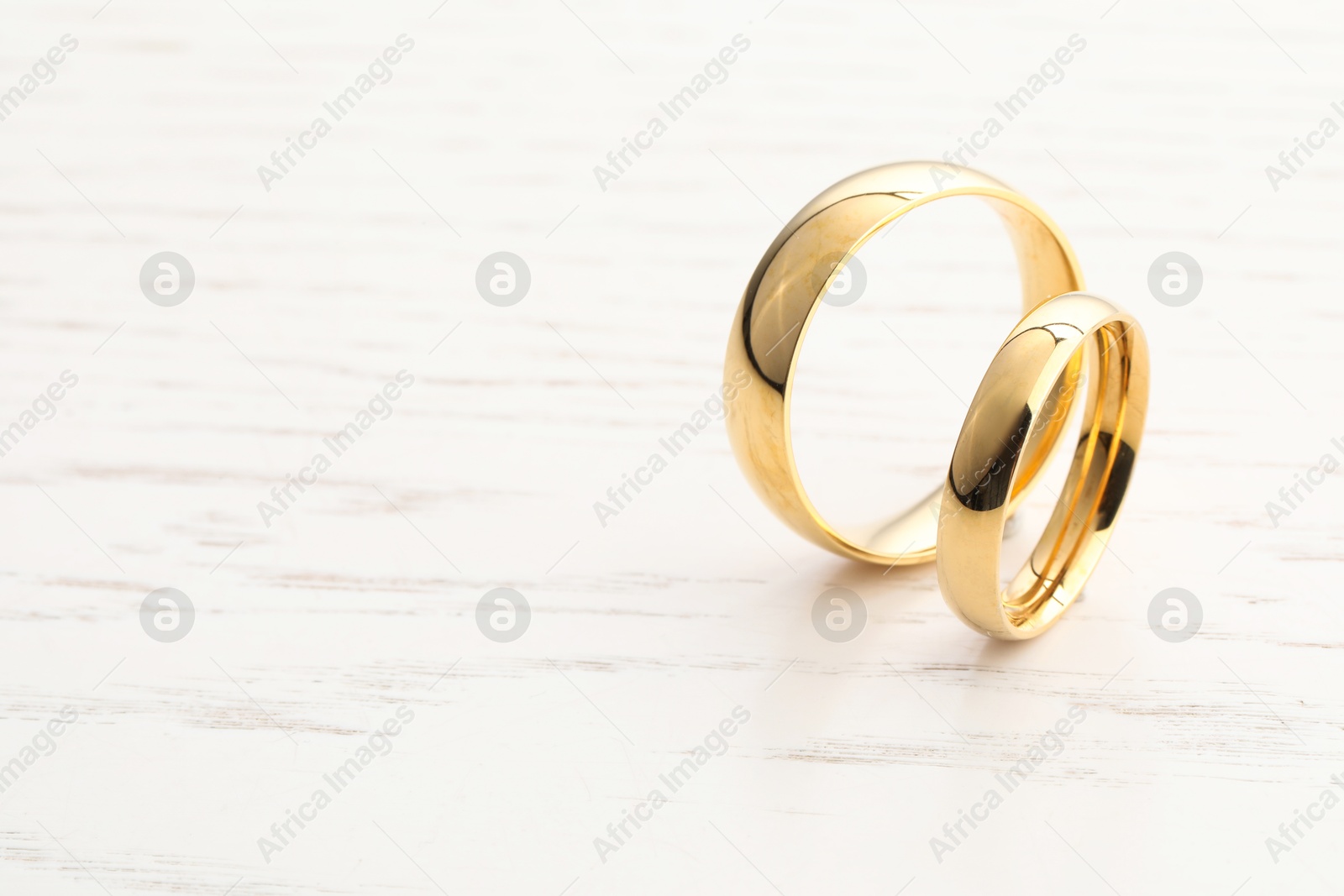 Photo of Beautiful golden wedding rings on light wooden background, space for text