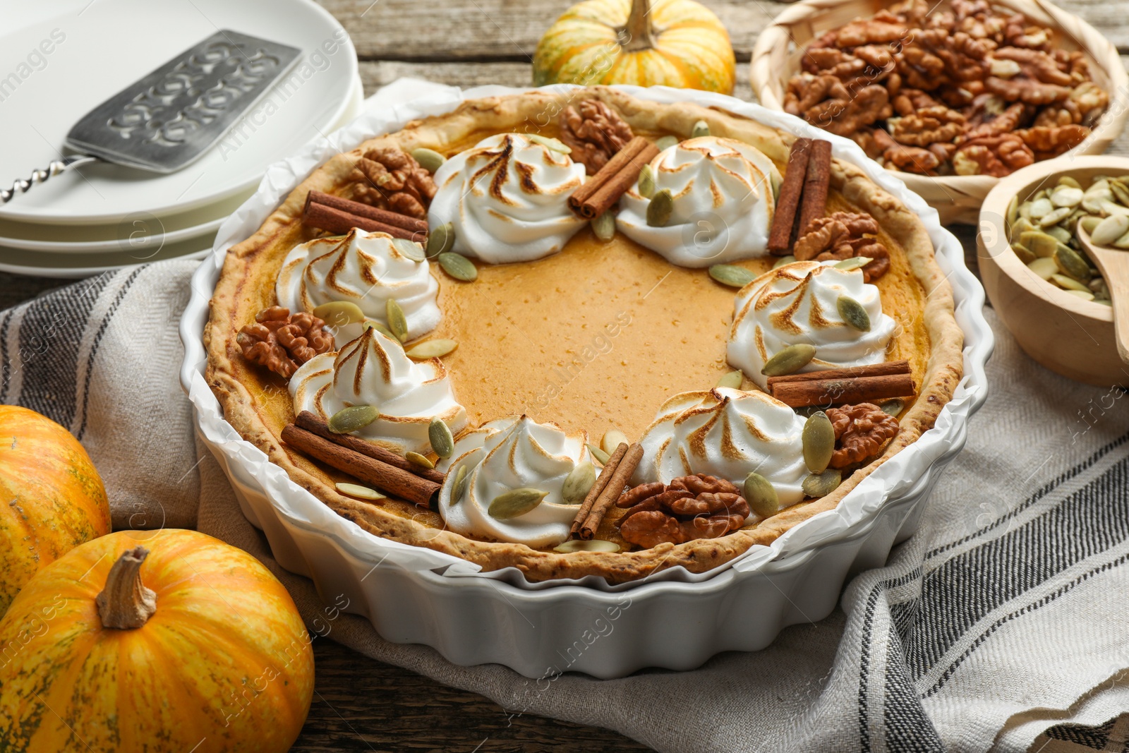 Photo of Tasty homemade pumpkin pie in baking dish and ingredients on wooden table, closeup