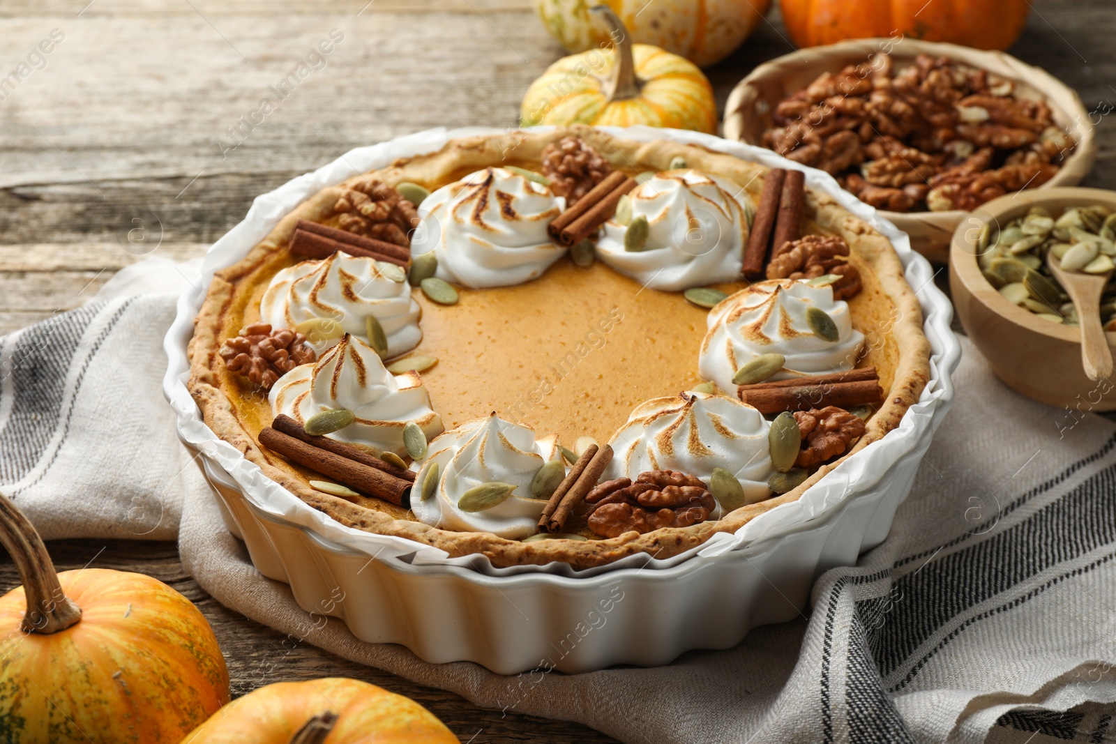 Photo of Tasty homemade pumpkin pie in baking dish and ingredients on wooden table, closeup