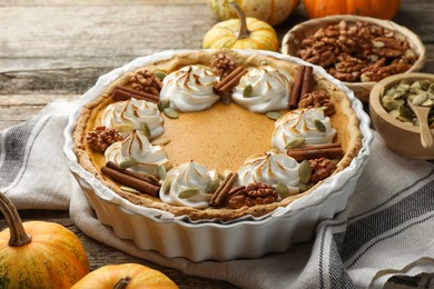 Photo of Tasty homemade pumpkin pie in baking dish and ingredients on wooden table, closeup