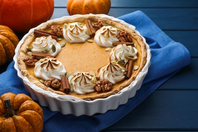 Photo of Delicious homemade pumpkin pie in baking dish and fresh pumpkins on blue wooden table, closeup