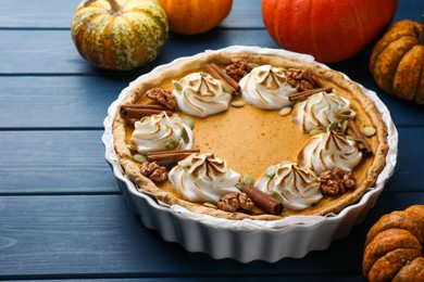 Photo of Delicious homemade pumpkin pie in baking dish and fresh pumpkins on blue wooden table, closeup