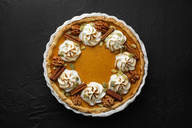 Photo of Delicious homemade pumpkin pie in baking dish on black textured table, top view