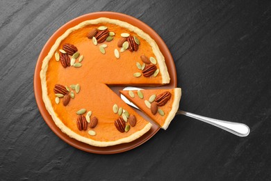 Photo of Tasty homemade pumpkin pie and server on black table, top view