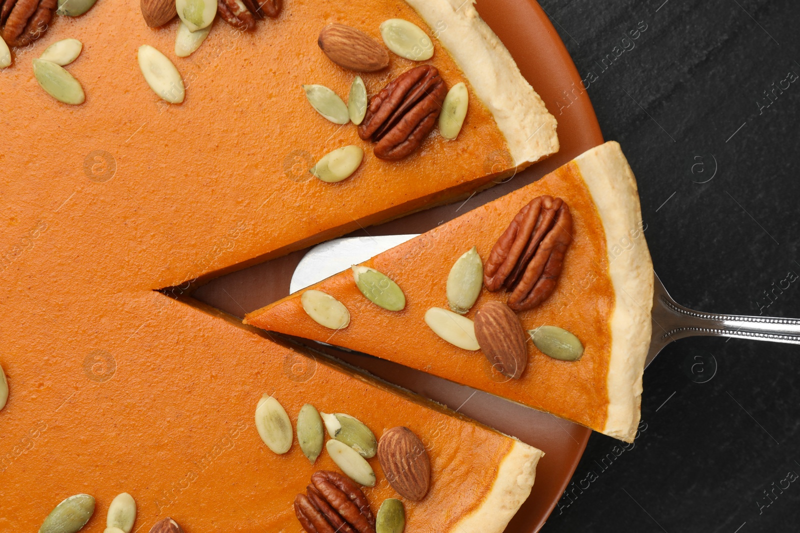 Photo of Taking piece of tasty homemade pumpkin pie at black table, top view