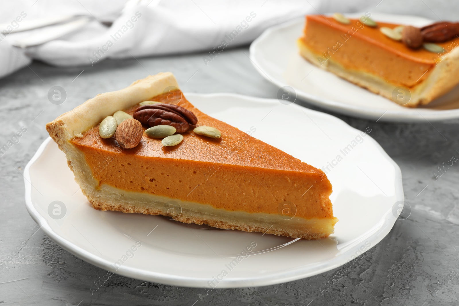 Photo of Pieces of tasty homemade pumpkin pie with seeds and nuts on grey table, closeup