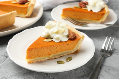 Photo of Pieces of tasty homemade pumpkin pie with whipped cream, seeds and nuts on grey table, closeup