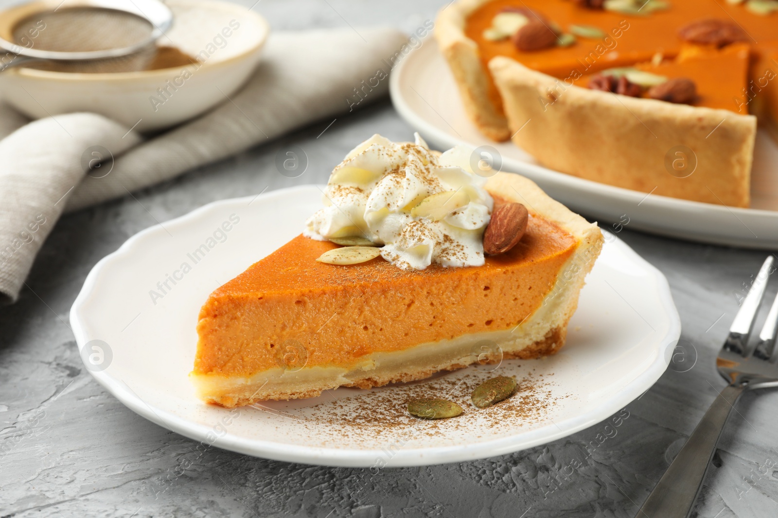 Photo of Piece of tasty homemade pumpkin pie with whipped cream, seeds and almond on grey table, closeup