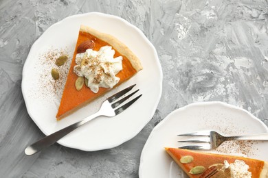 Photo of Pieces of tasty homemade pumpkin pie with whipped cream and seeds on grey table, top view