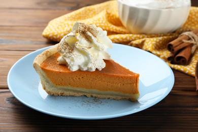 Photo of Piece of tasty homemade pumpkin pie with whipped cream on wooden table, closeup