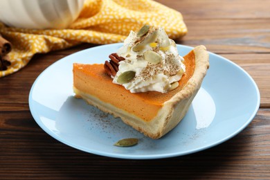 Photo of Piece of tasty homemade pumpkin pie with whipped cream, seeds and pecan nut on wooden table, closeup