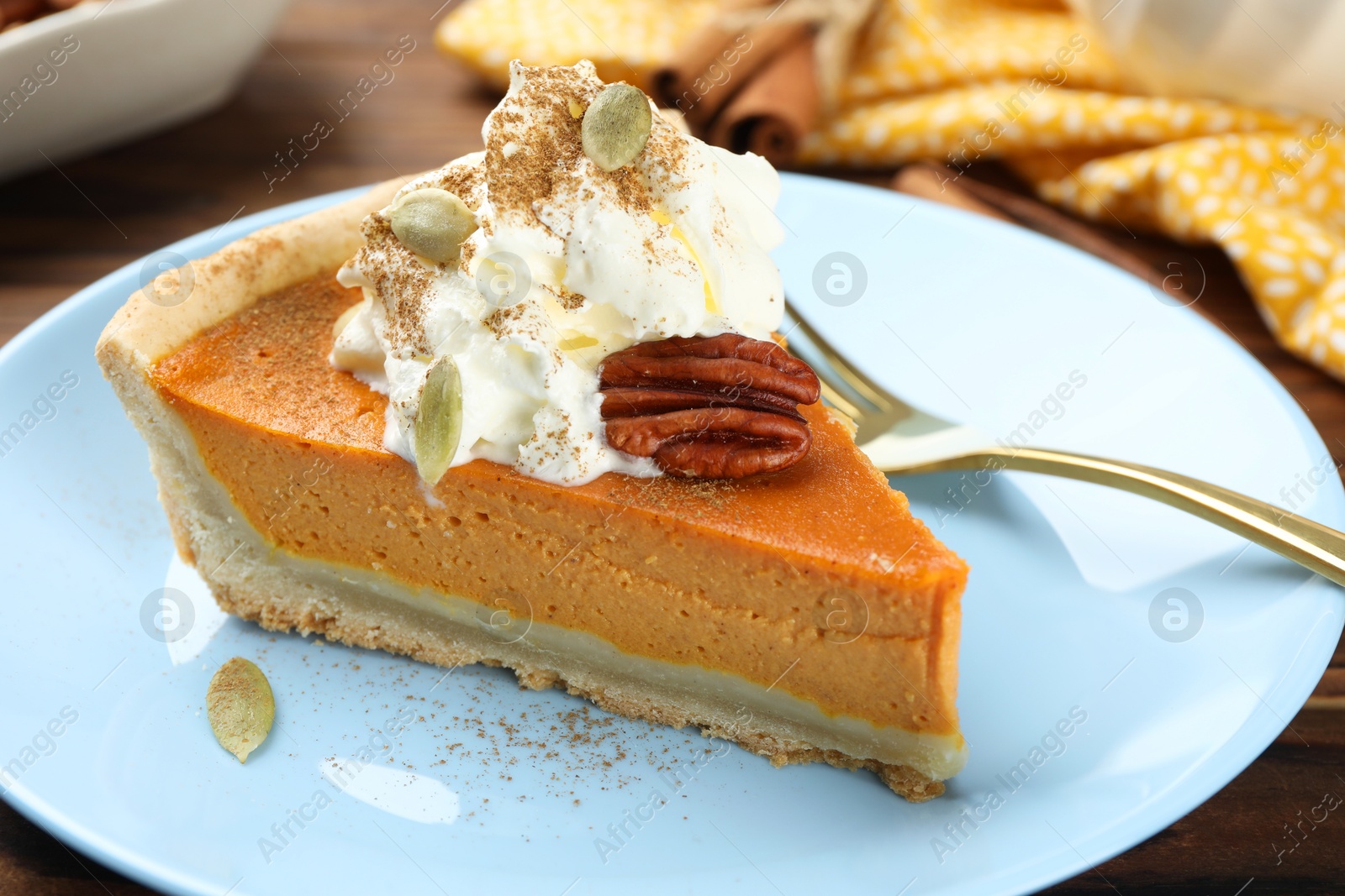 Photo of Piece of tasty homemade pumpkin pie with whipped cream, seeds and pecan nut on table, closeup