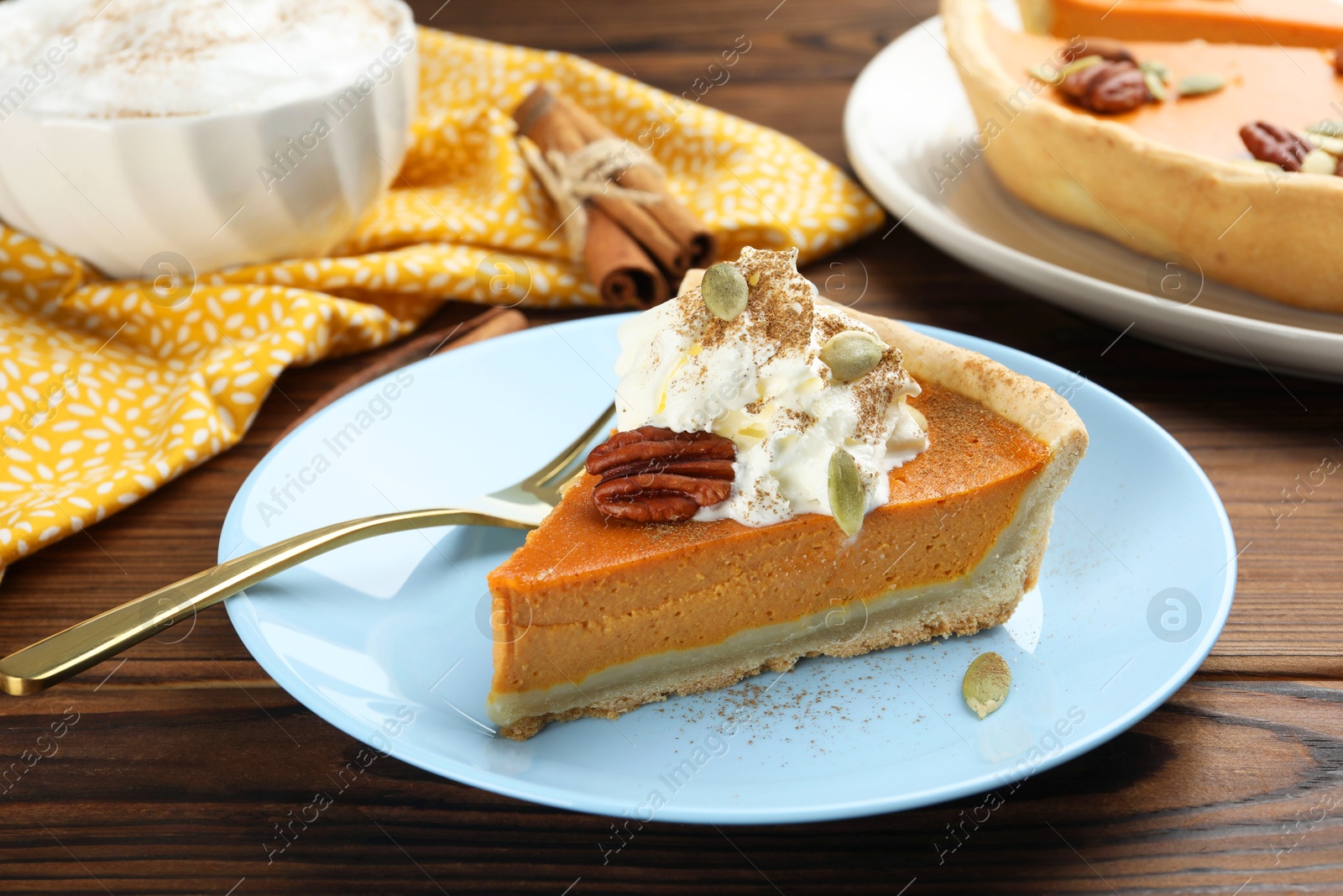 Photo of Piece of tasty homemade pumpkin pie with whipped cream, seeds and pecan nut on wooden table, closeup