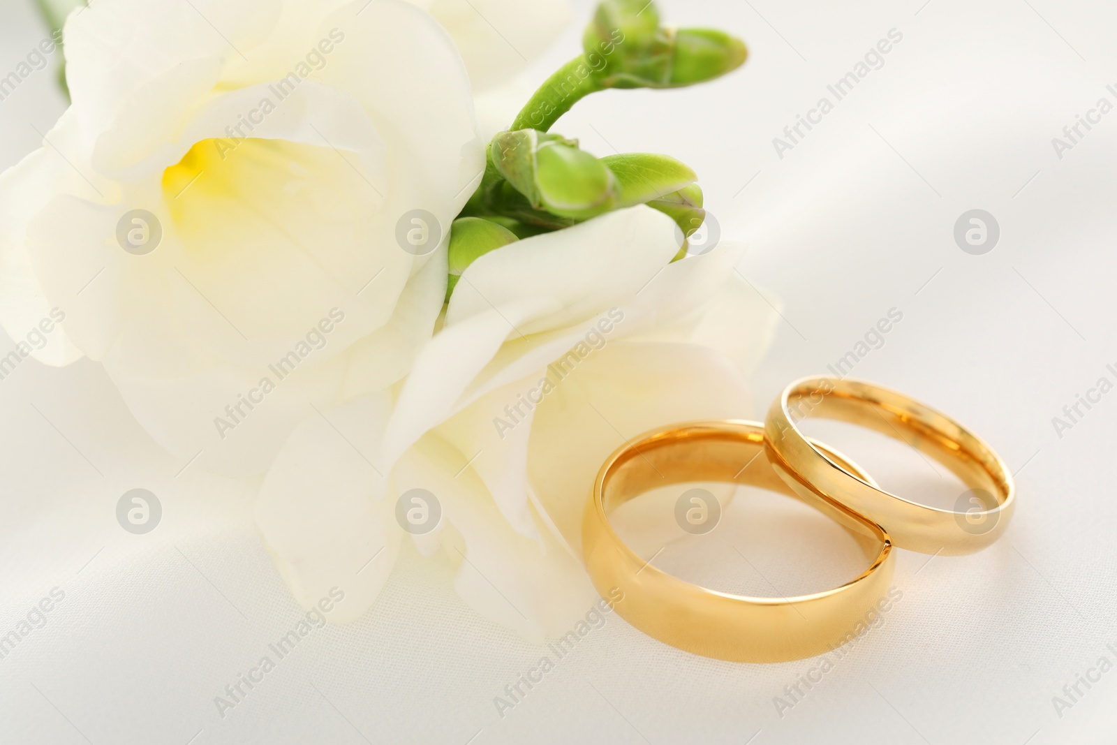 Photo of Golden wedding rings and flowers on white fabric, closeup