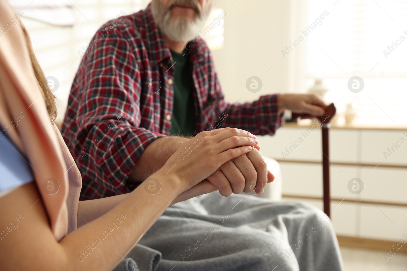 Photo of Caregiver supporting senior man on sofa indoors, closeup. Home health care service