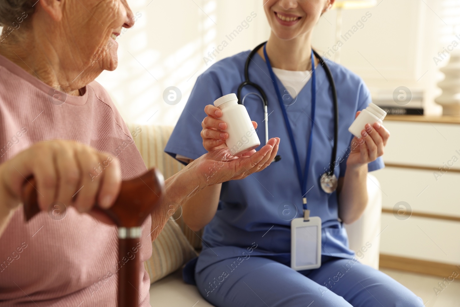 Photo of Caregiver giving pills to senior woman on sofa indoors, closeup. Home health care service