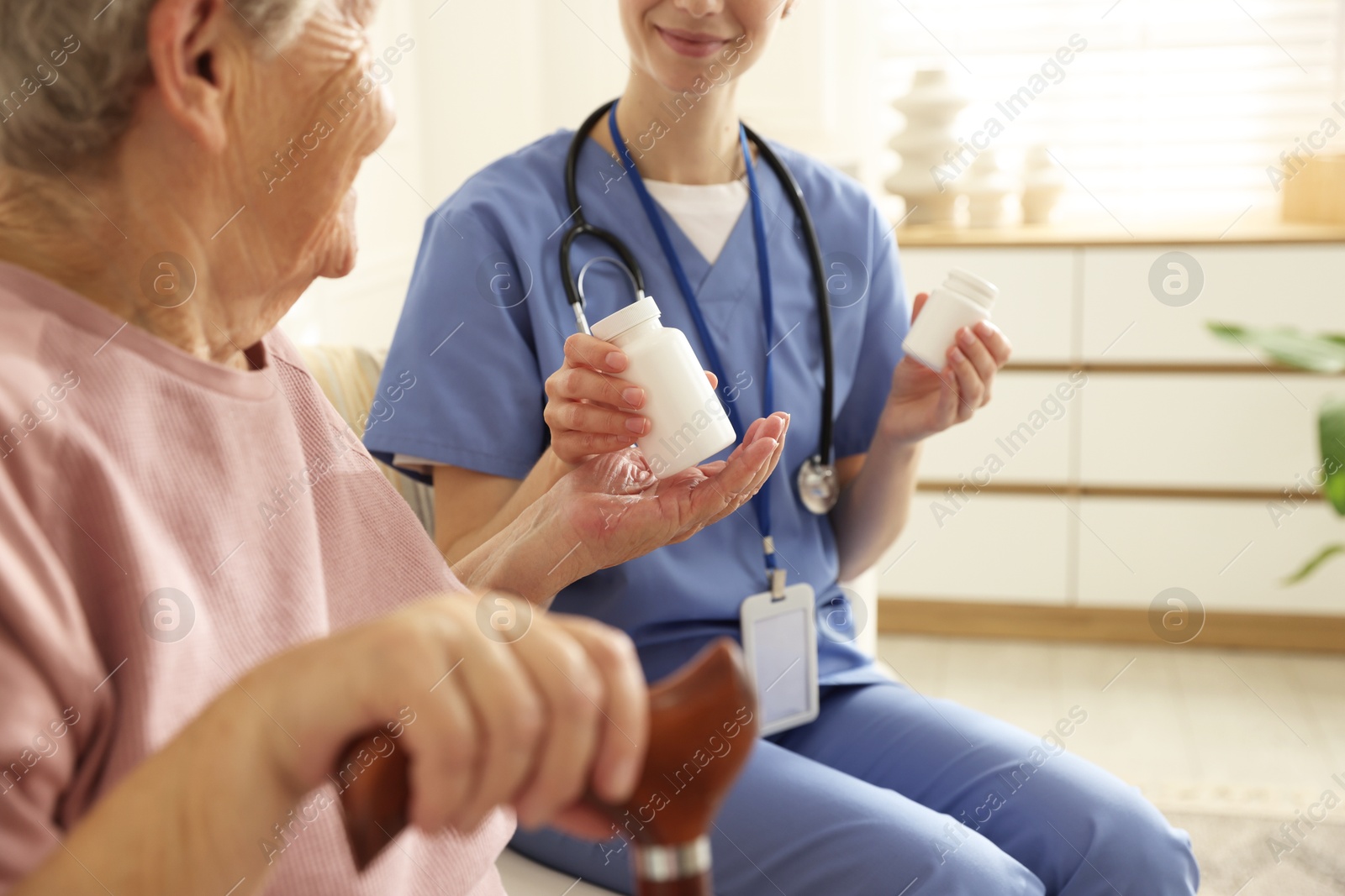 Photo of Caregiver giving pills to senior woman on sofa indoors, closeup. Home health care service