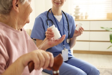 Photo of Caregiver giving pills to senior woman on sofa indoors, closeup. Home health care service