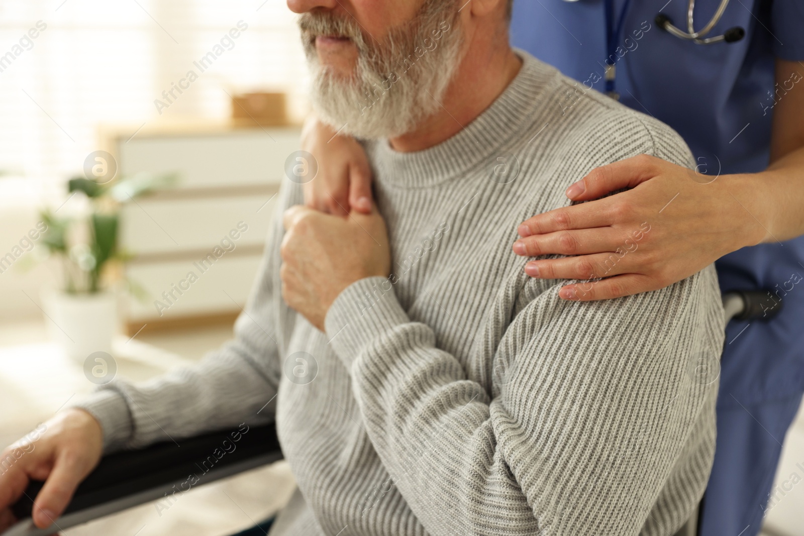 Photo of Caregiver assisting senior man in wheelchair indoors, closeup. Home health care service