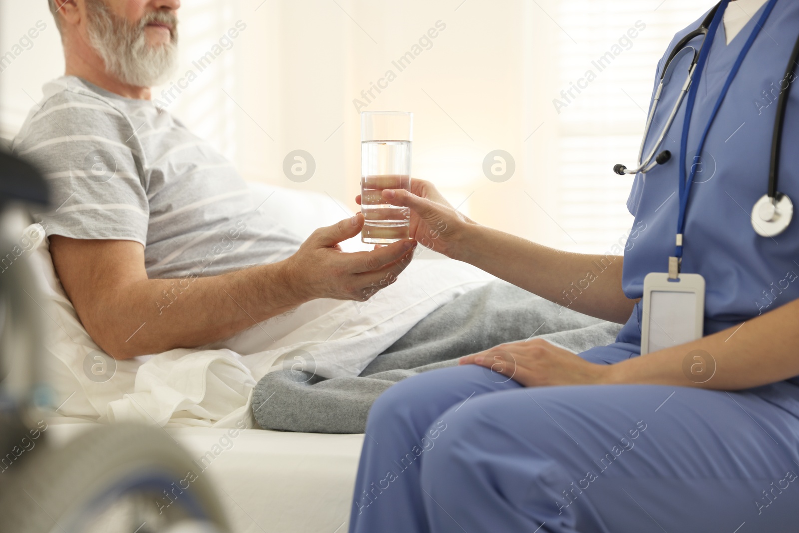 Photo of Caregiver giving water to senior man on bed indoors, closeup. Home health care service