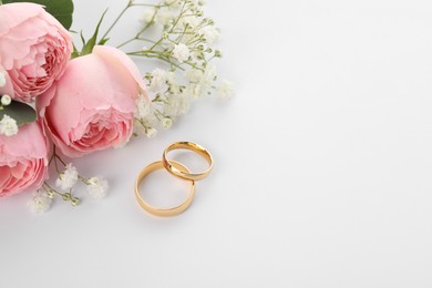 Photo of Golden wedding rings and flowers on white background. Space for text