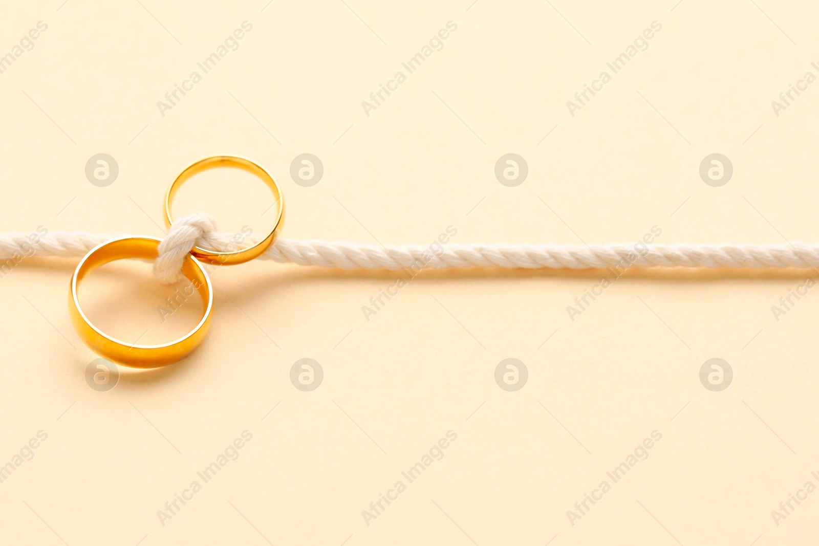 Photo of Golden wedding rings tied with string on beige background, closeup