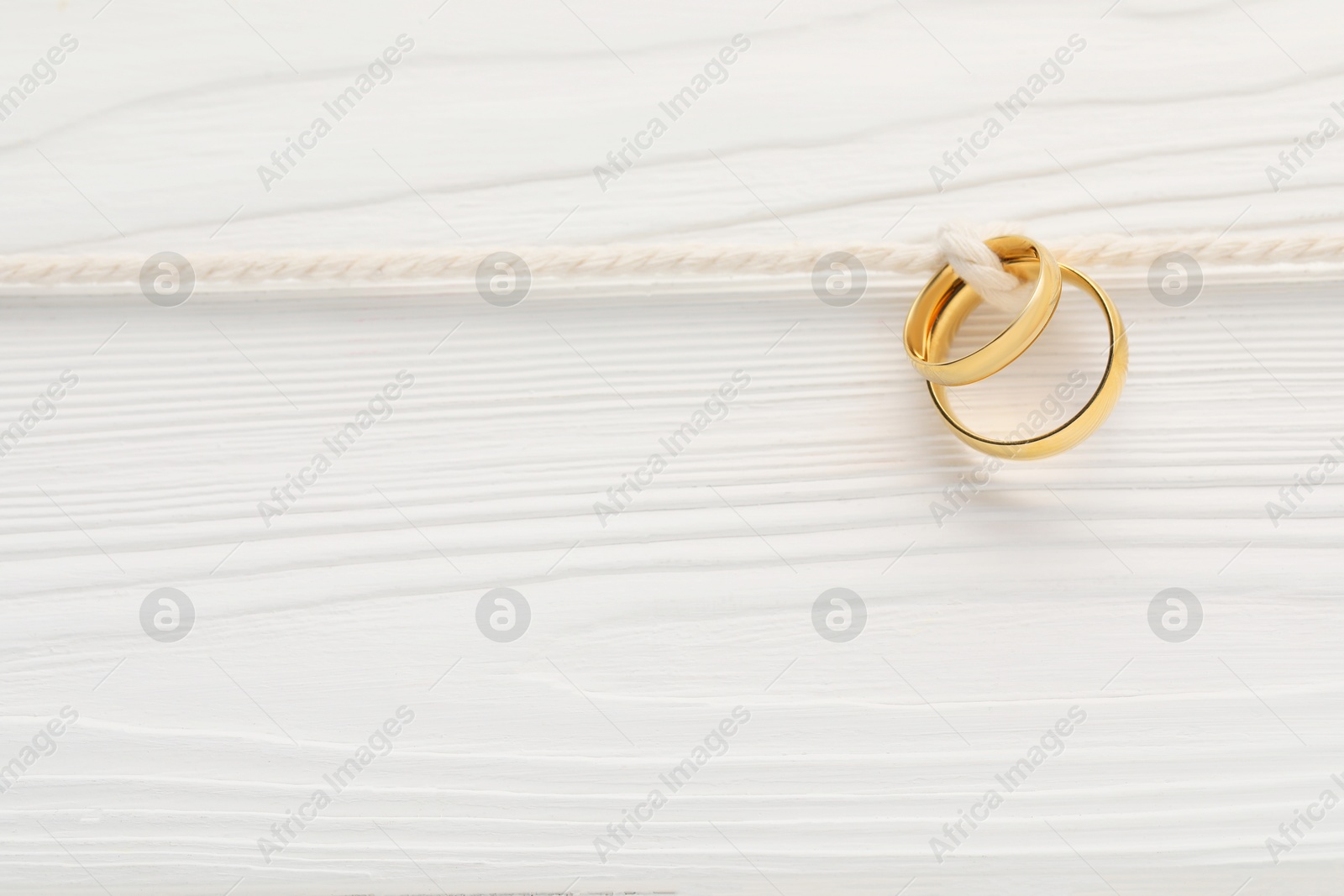 Photo of Golden wedding rings tied with string on white wooden background, above view