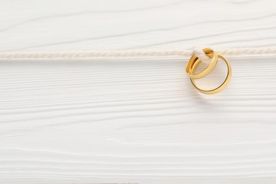 Photo of Golden wedding rings tied with string on white wooden background, above view