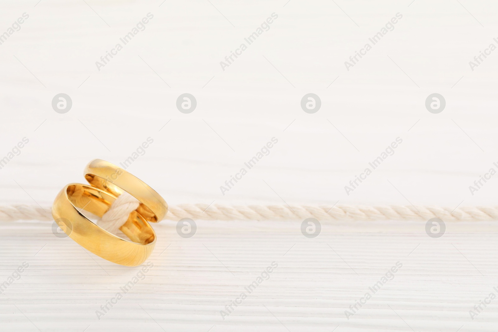 Photo of Golden wedding rings tied with string on white wooden background, closeup. Space for text