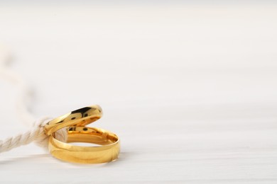 Photo of Golden wedding rings tied with string on white wooden background, closeup. Space for text