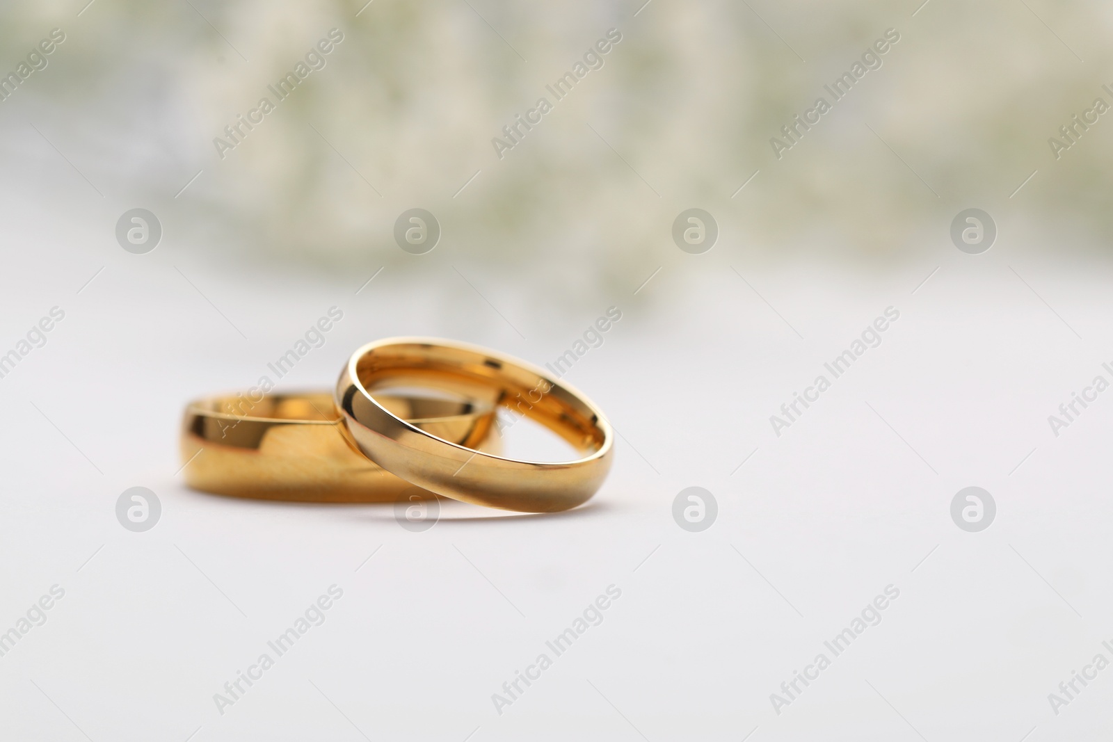 Photo of Golden wedding rings on white background, closeup. Space for text