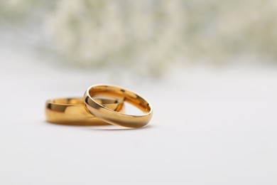 Photo of Golden wedding rings on white background, closeup. Space for text