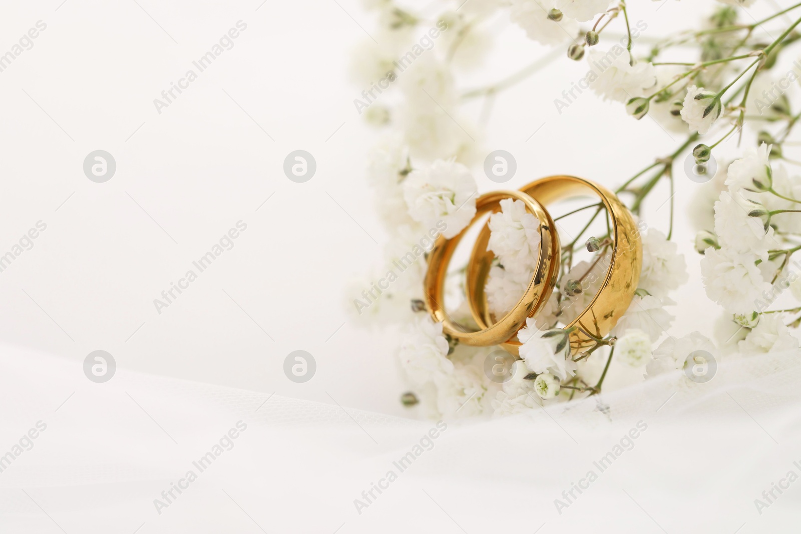 Photo of Golden wedding rings, veil and flowers on blurred background, closeup. Space for text