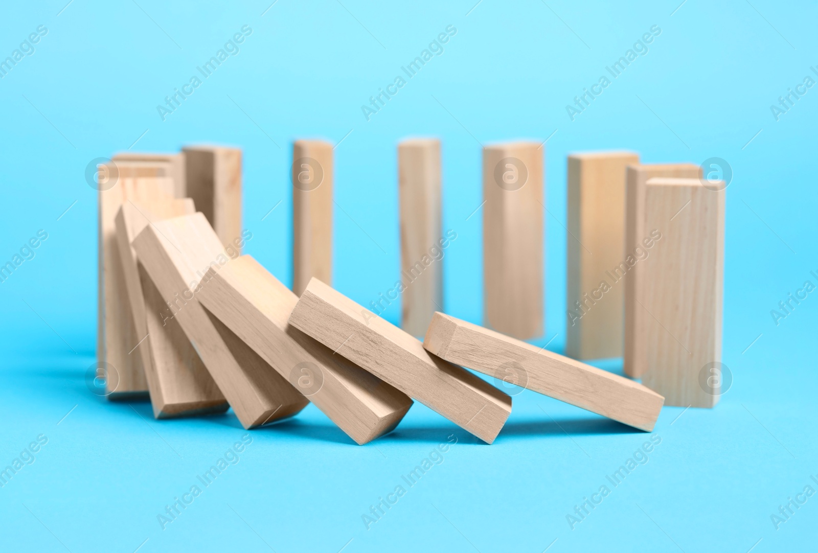 Photo of Domino effect. Wooden blocks falling on light blue background