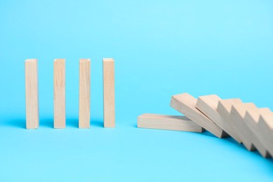 Photo of Domino effect. Wooden blocks falling on light blue background