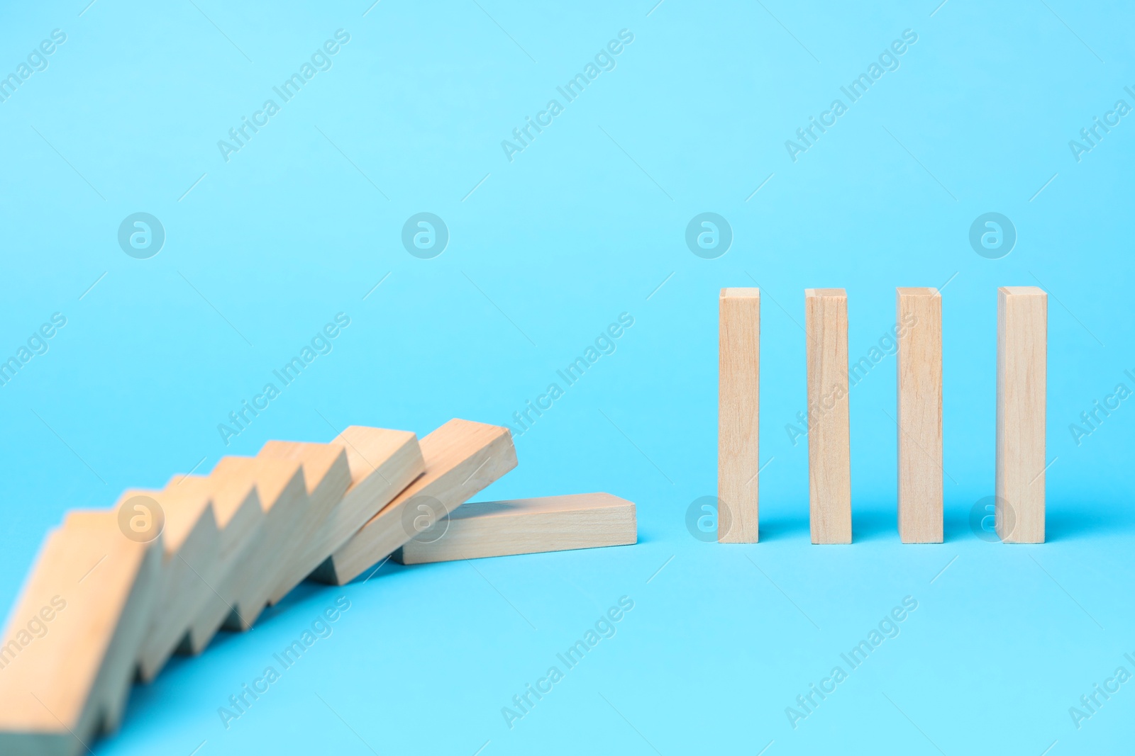 Photo of Domino effect. Wooden blocks falling on light blue background