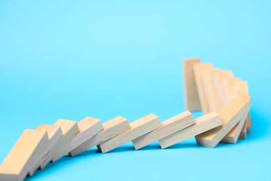 Photo of Domino effect. Wooden blocks falling on light blue background