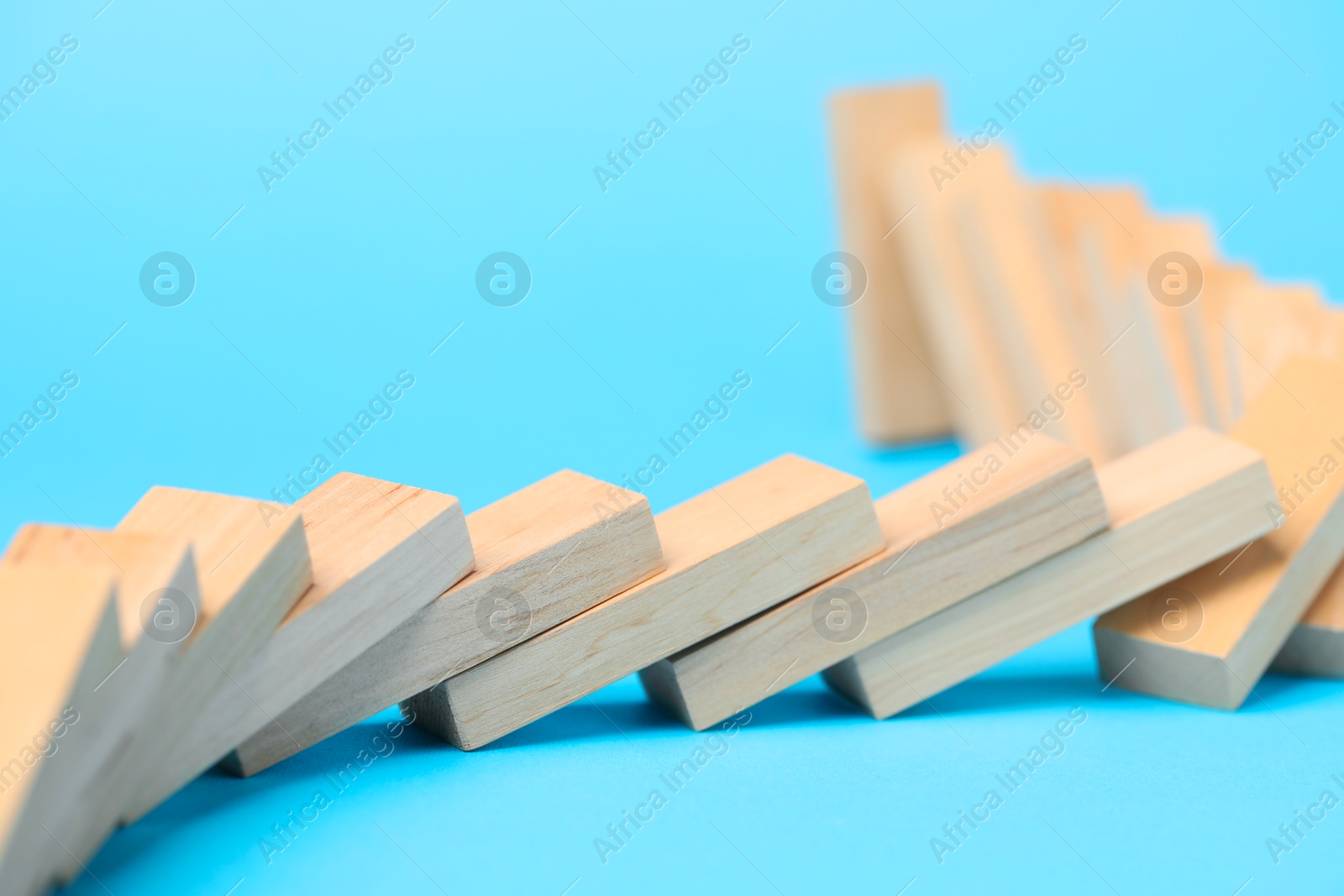 Photo of Domino effect. Wooden blocks falling on light blue background, closeup