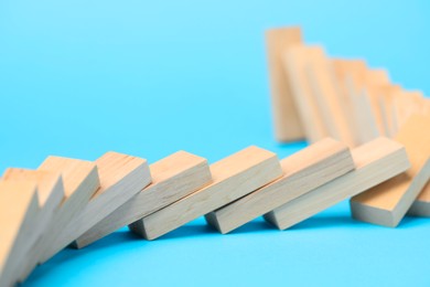 Photo of Domino effect. Wooden blocks falling on light blue background, closeup