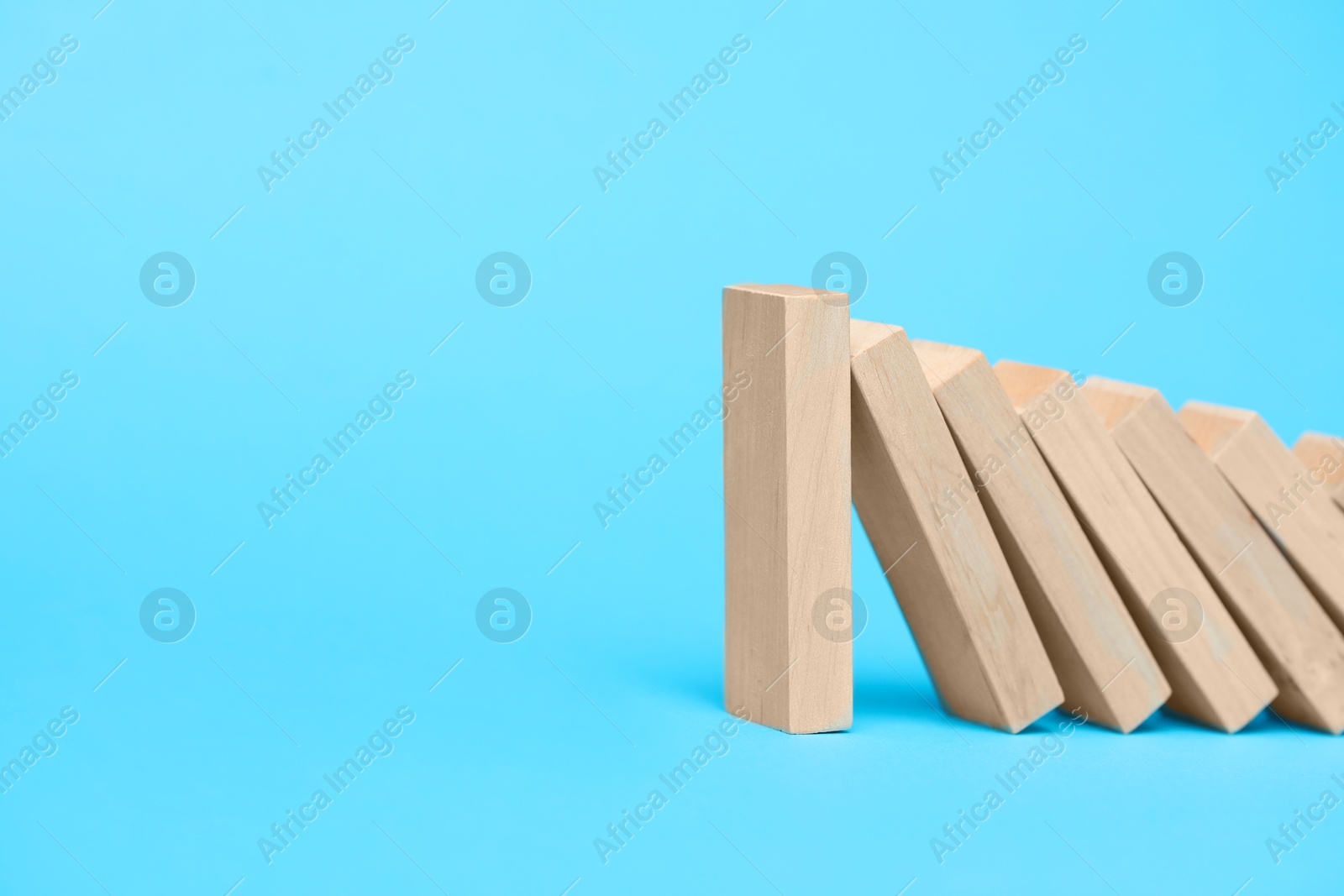 Photo of Domino effect. Wooden blocks falling on light blue background. Space for text