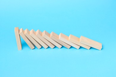 Photo of Domino effect. Wooden blocks falling on light blue background