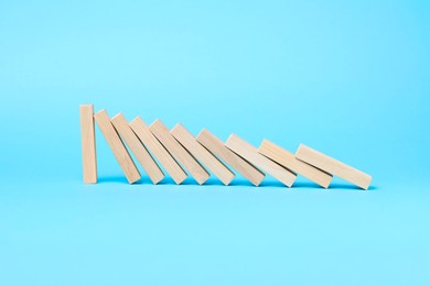 Photo of Domino effect. Wooden blocks falling on light blue background. Space for text