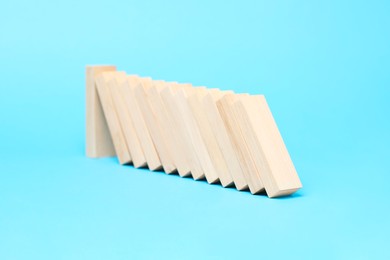 Photo of Domino effect. Wooden blocks falling on light blue background