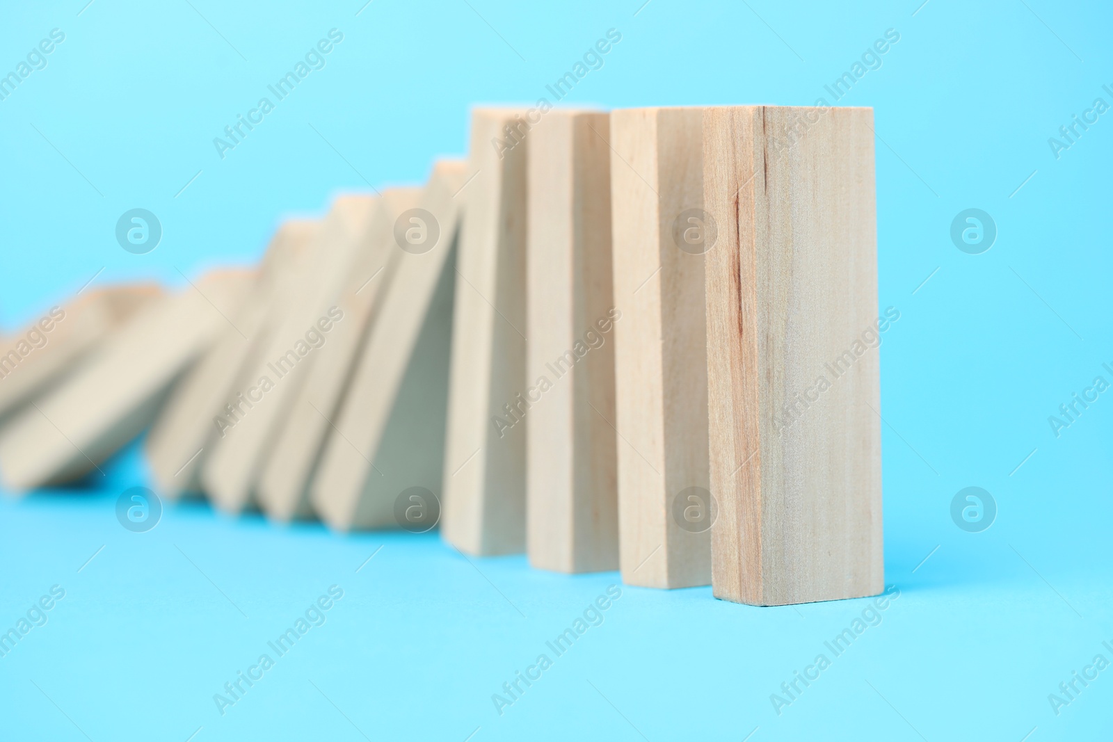 Photo of Domino effect. Wooden blocks falling on light blue background, closeup