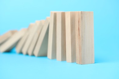 Photo of Domino effect. Wooden blocks falling on light blue background, closeup