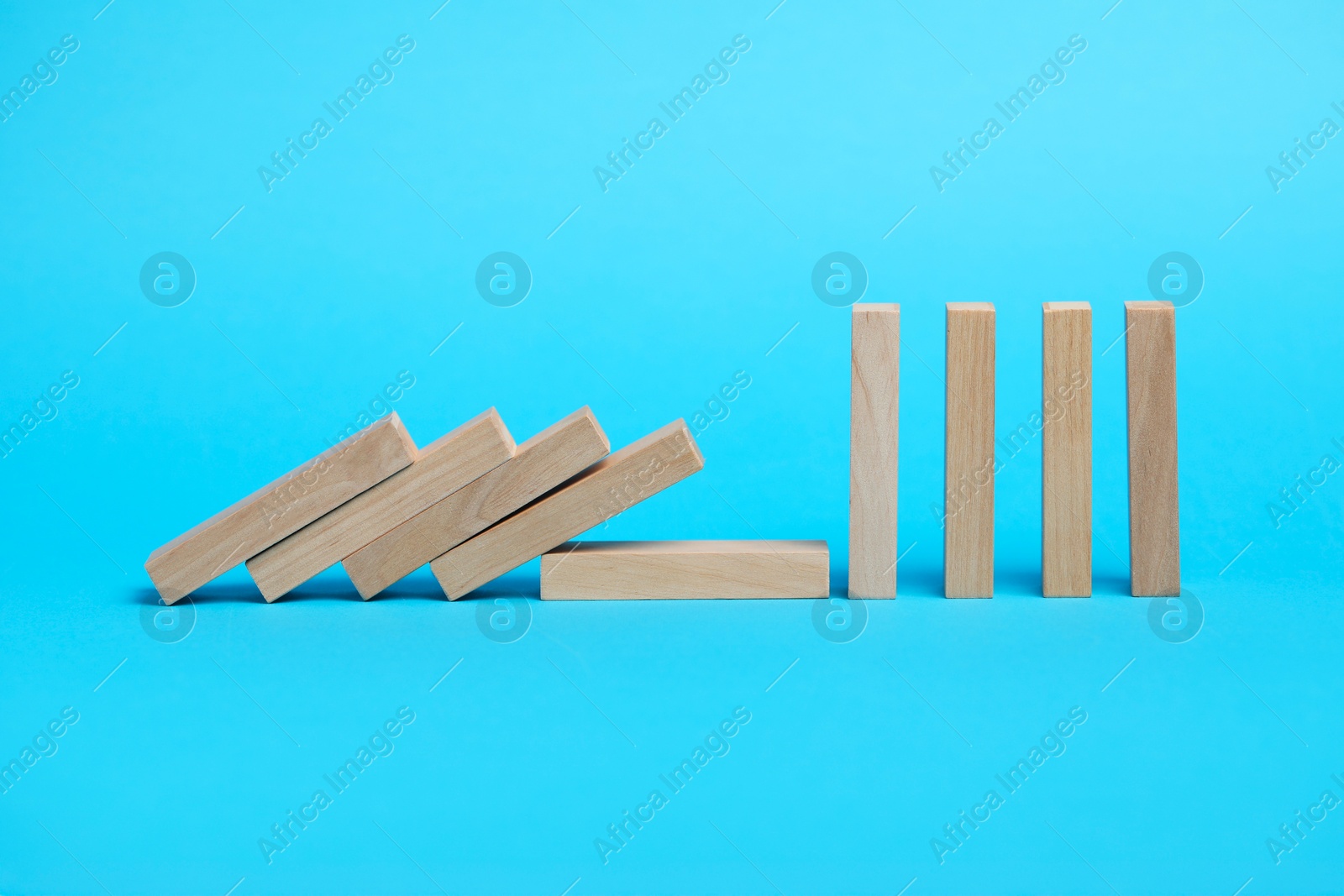 Photo of Domino effect. Wooden blocks falling on light blue background