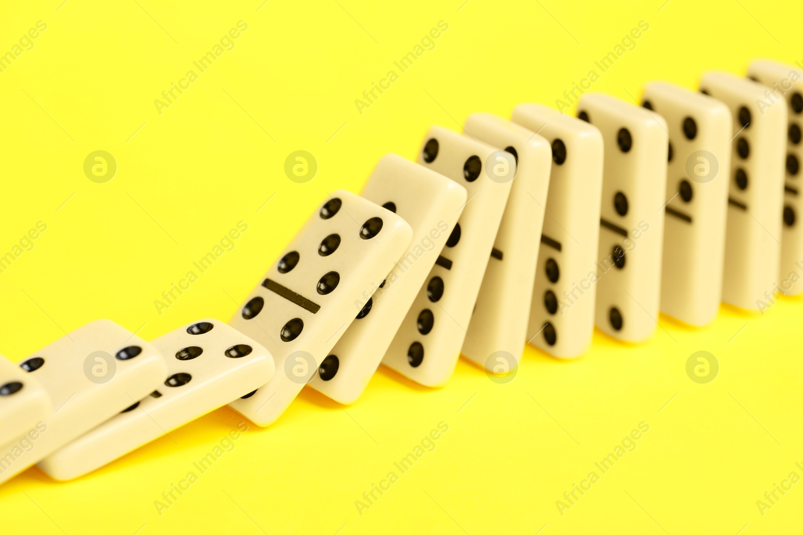 Photo of Domino effect. Tiles falling on yellow background, closeup