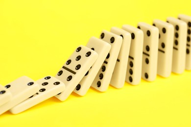 Photo of Domino effect. Tiles falling on yellow background, closeup