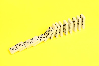 Photo of Domino effect. Tiles falling on yellow background